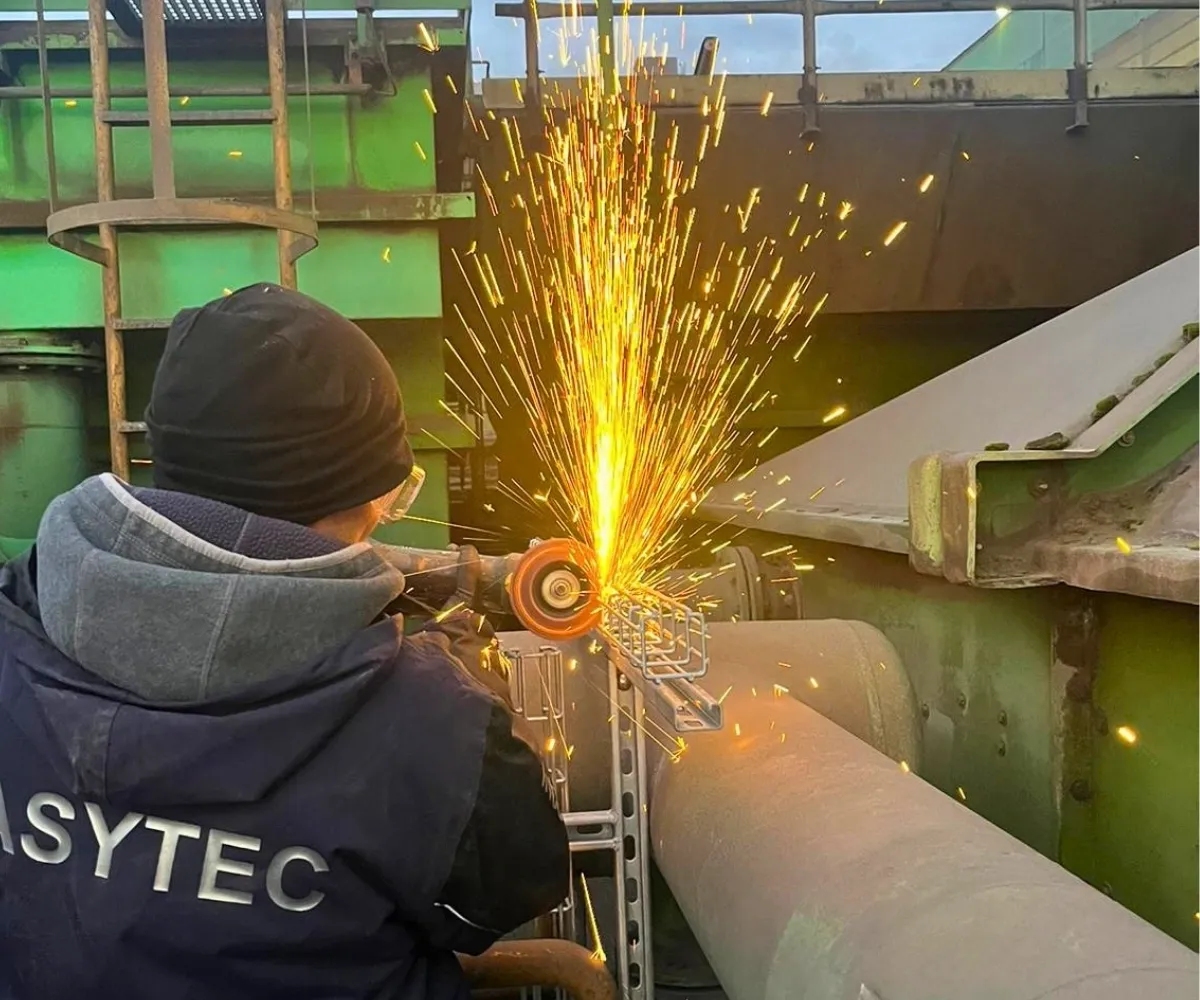 Monteur trennt mit dem Winkelschleifer ein Metallteil an einer Industrieanlage, Funken fliegen